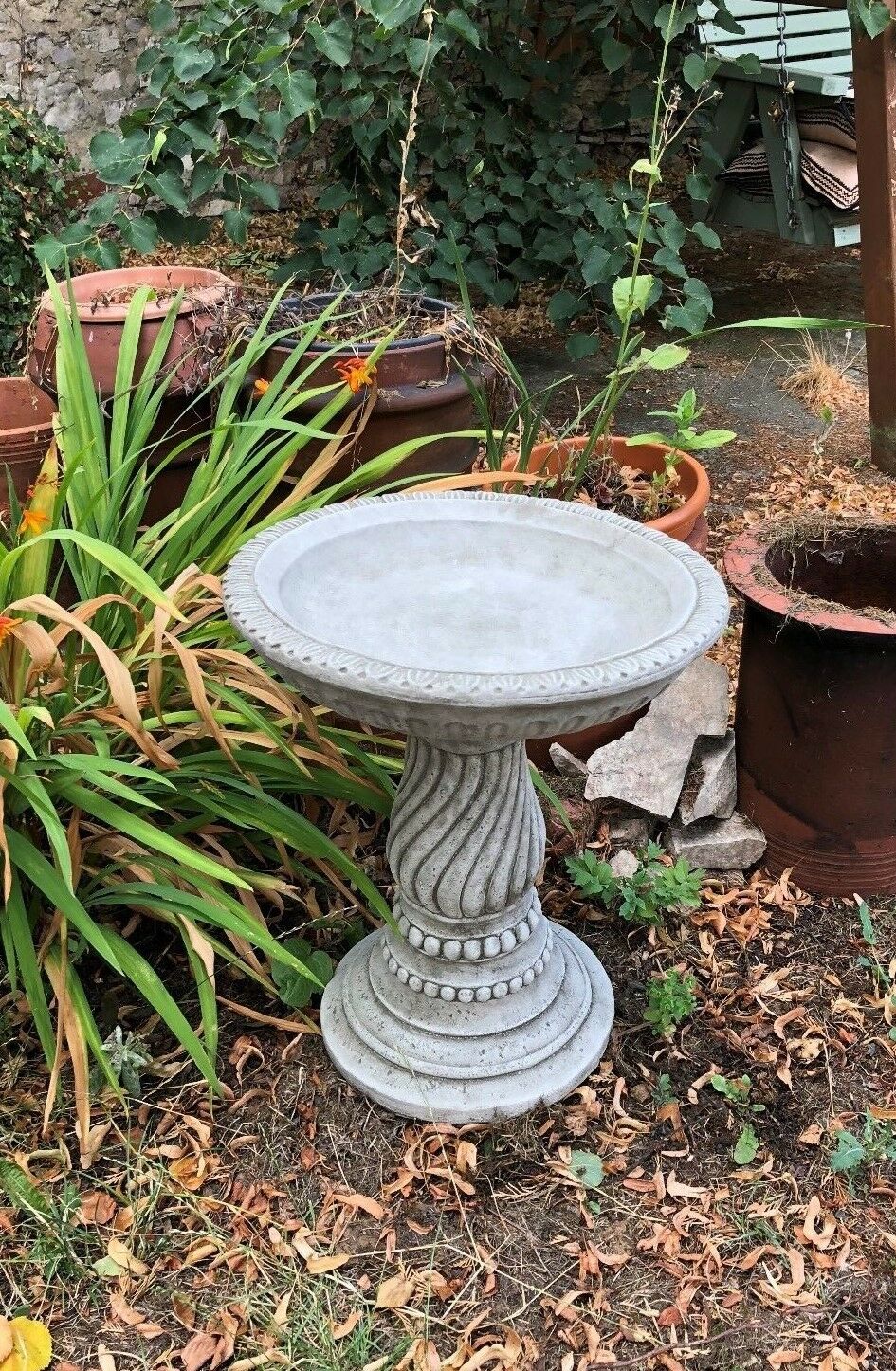 Elegant stone garden bird bath with twisted pedestal base in a rustic garden setting. Perfect for attracting birds to your patio or lawn.