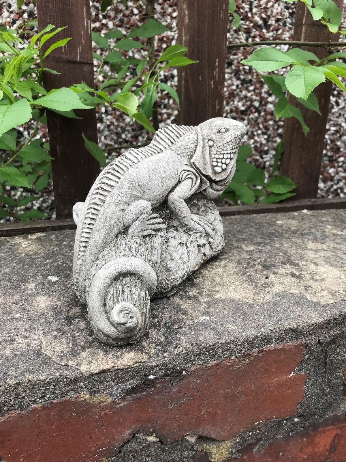 Handcrafted iguana ornament in durable stone, resting on a garden wall, from the Iguana Garden Ornaments - Stone Collection.