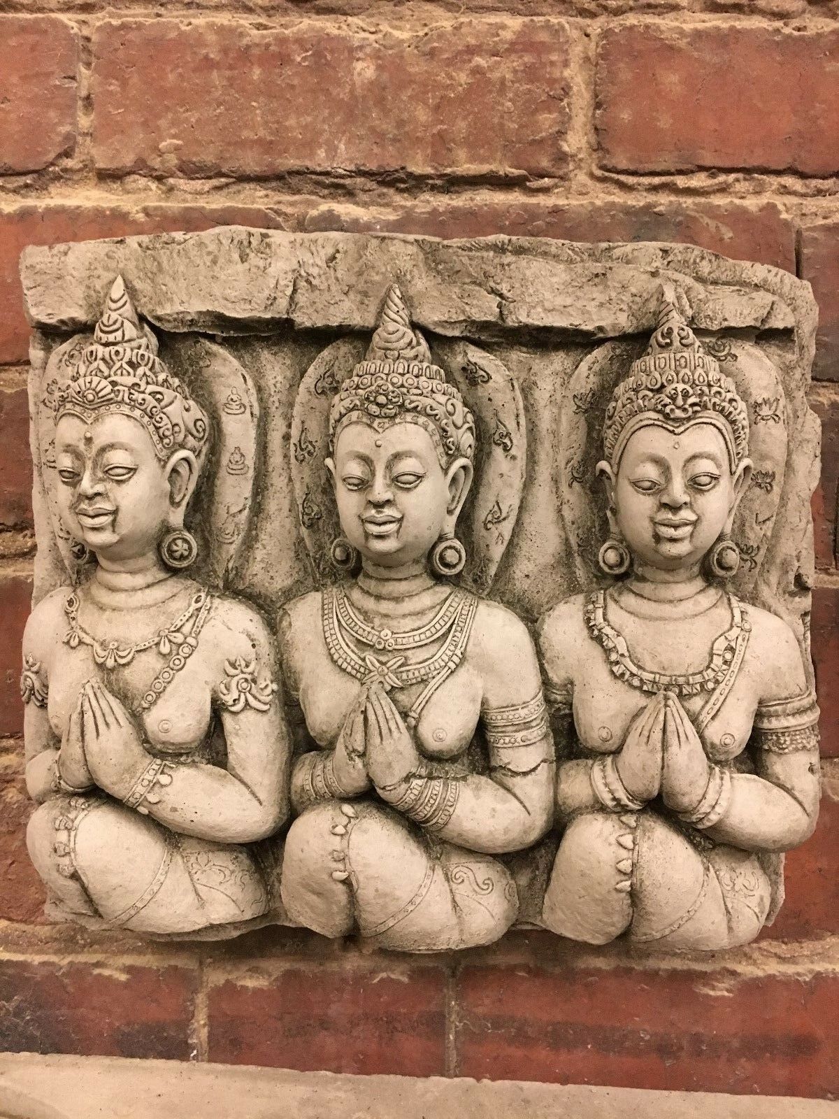 Stone Buddha wall plaque featuring three intricately carved figures in prayer pose. Ideal for garden decor, made from durable limestone.