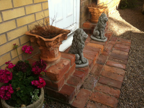Pair of stone lion statues flanking a front door on brick steps, creating a grand entrance with timeless garden decor.