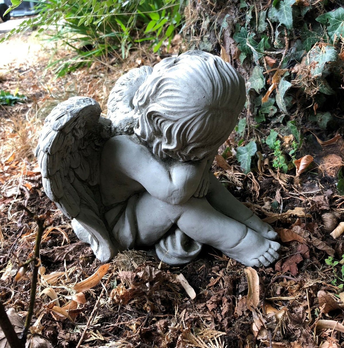Side angle of sleeping stone baby angel with folded arms and wings. Ideal for tranquil garden corners or spiritual outdoor accents.