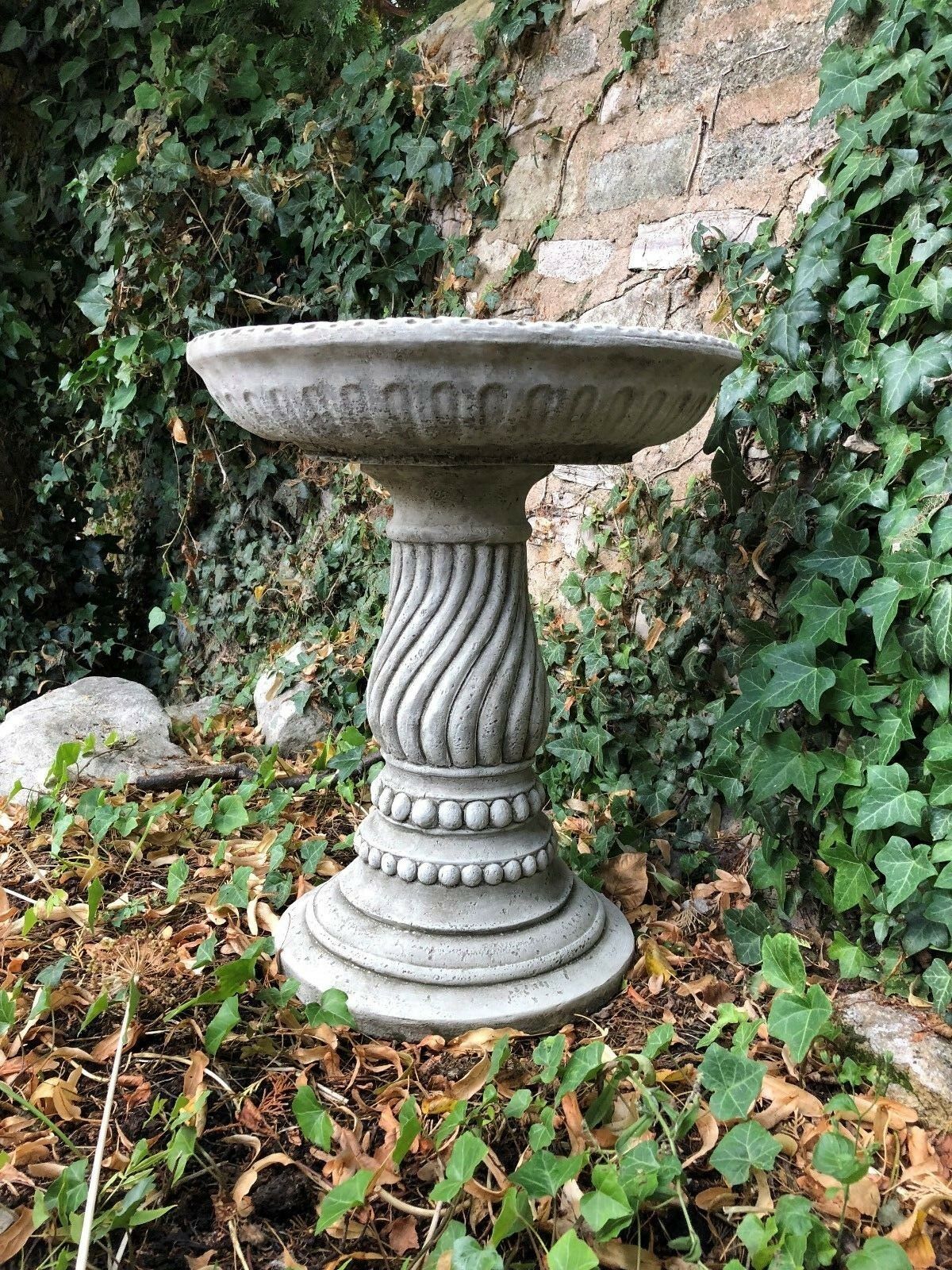 Twist base stone bird bath in a natural garden corner, crafted from solid limestone for year-round outdoor use. Free UK delivery available.