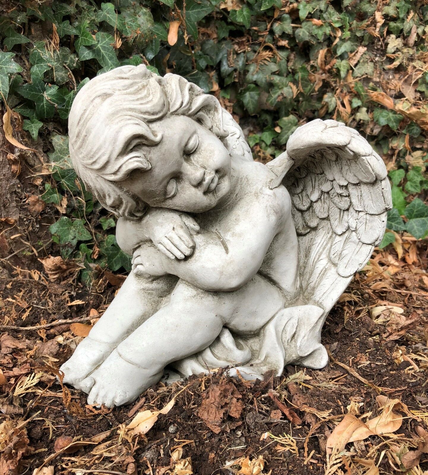 Resting stone cherub angel with serene expression and detailed wings. Handmade sculpture for garden, patio, or grave site decor.