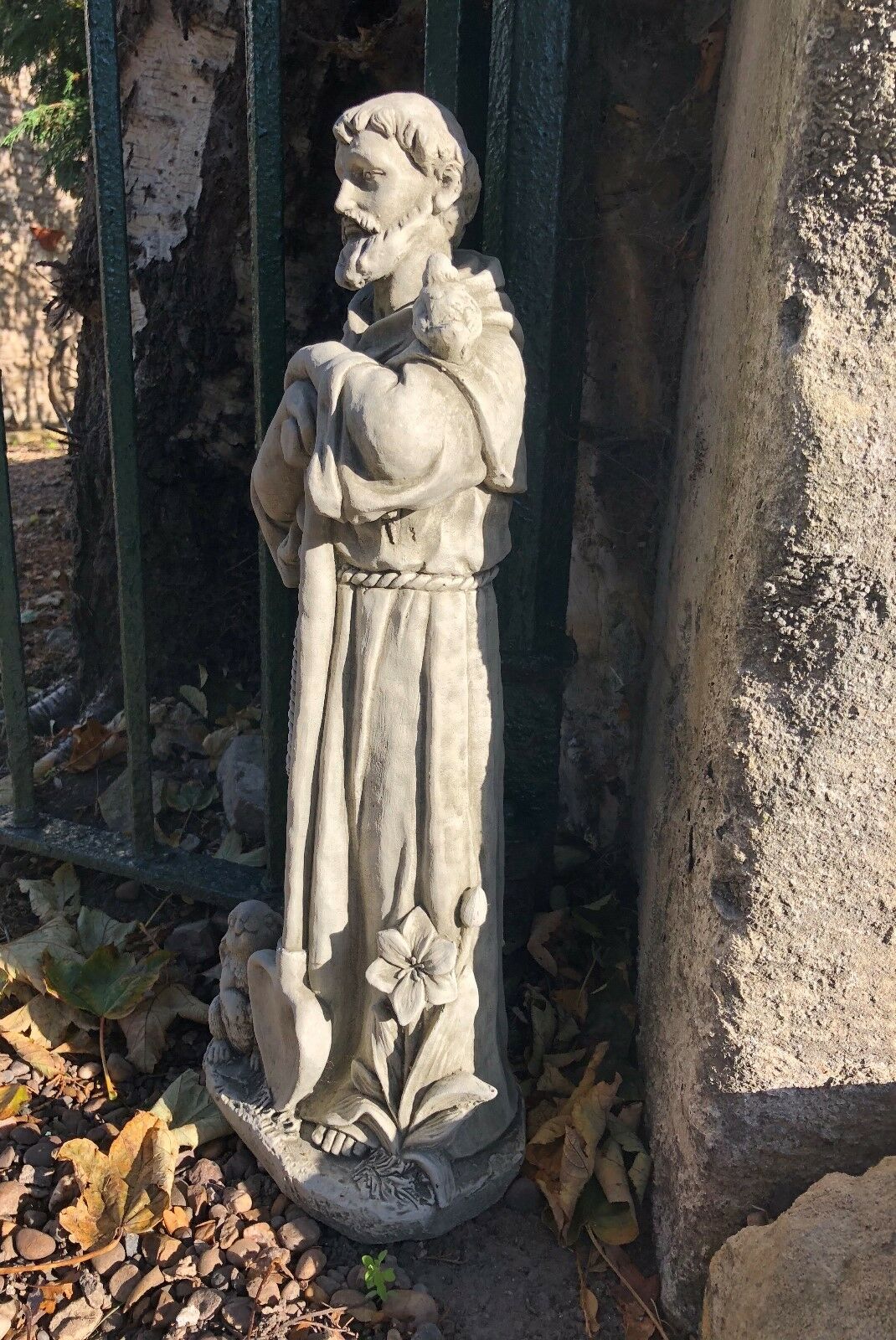 Side view of St Francis stone statue showing floral and animal details. Durable garden sculpture for outdoor religious or decorative use.