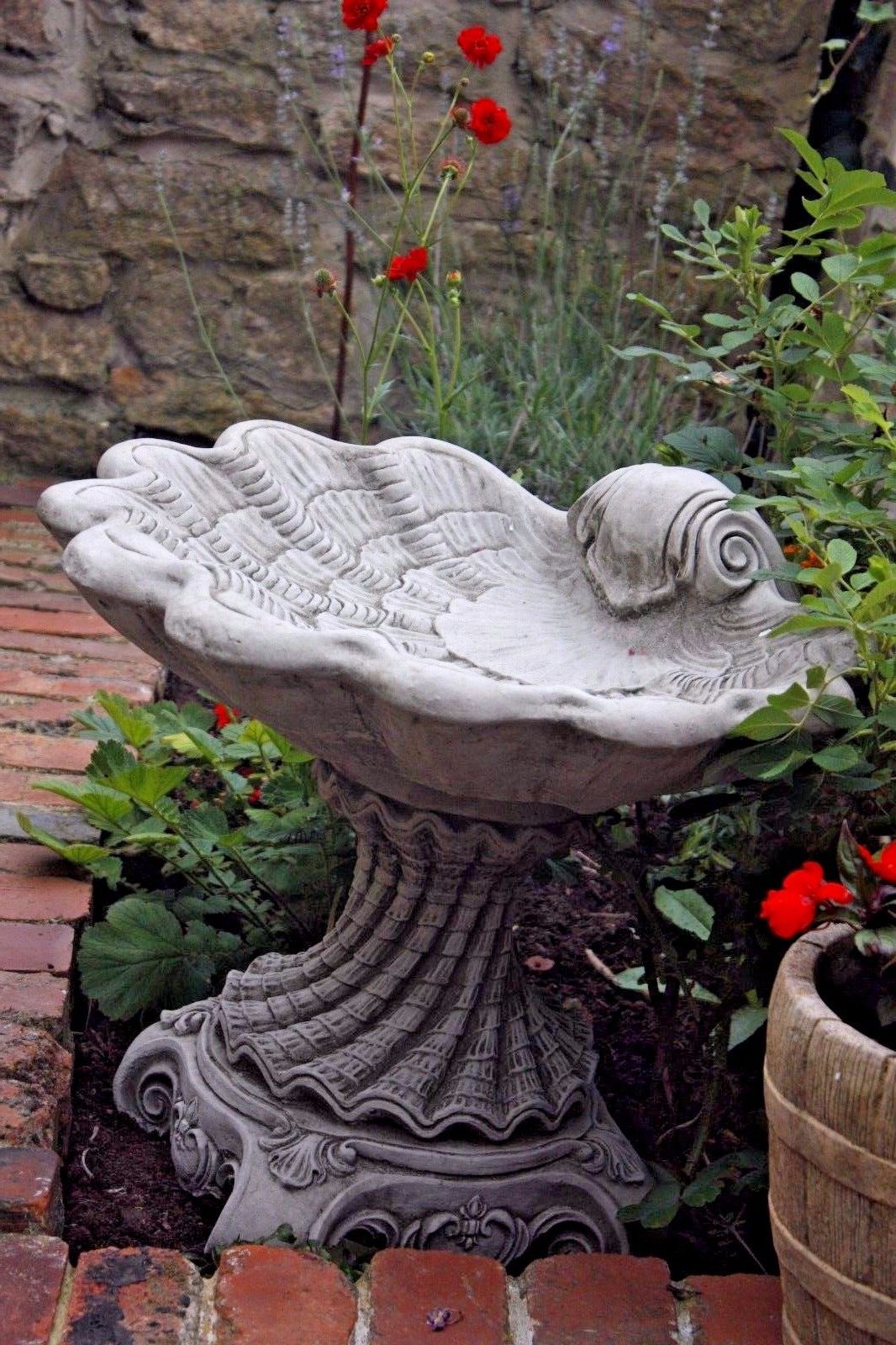Elegant Stone Shell Bird Bath placed among red flowers and greenery, perfect for enhancing garden aesthetics and attracting birds.