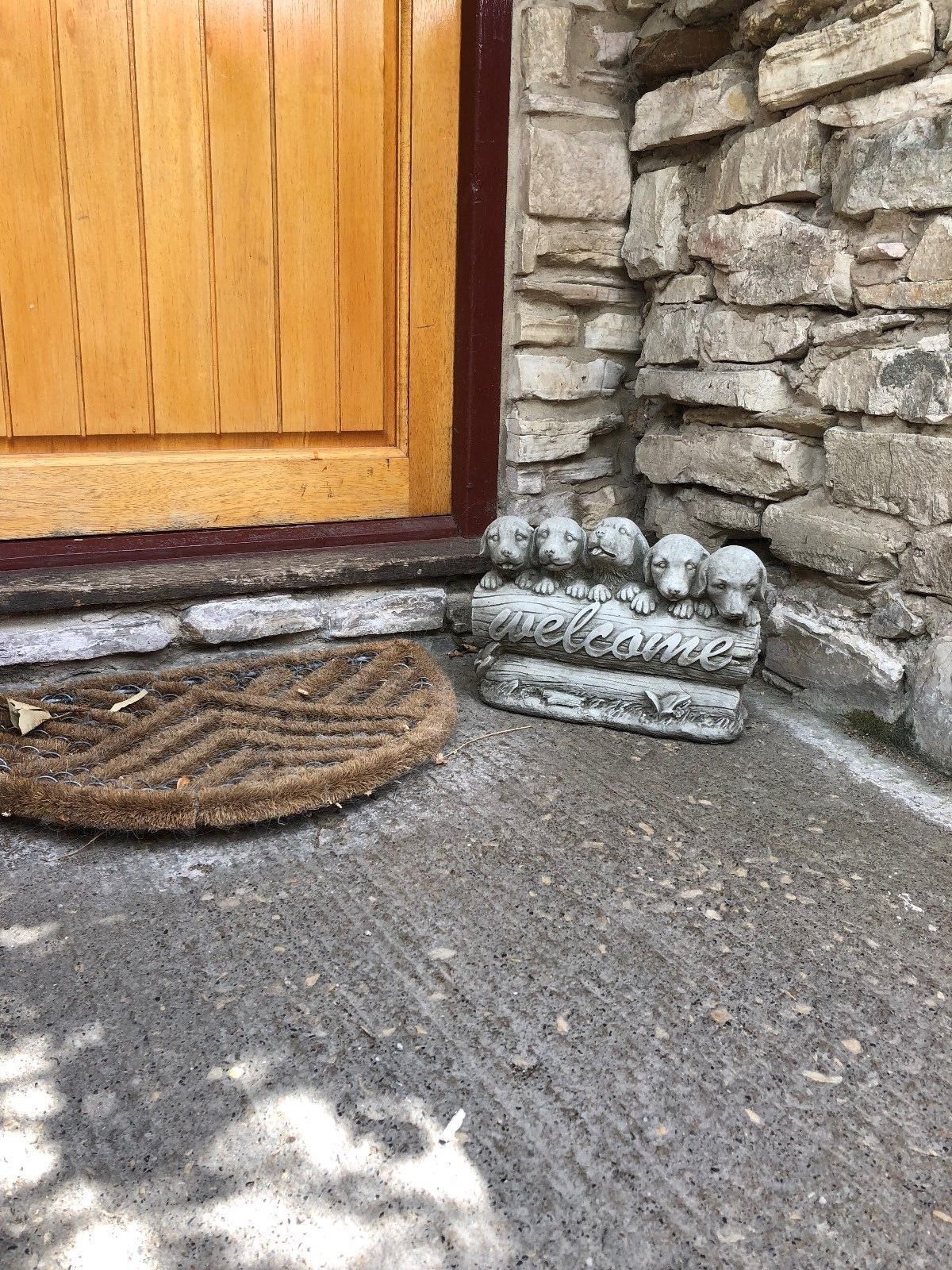 Stone Welcome Puppies ornament placed near a front door, enhancing entryway charm with rustic garden decor appeal.