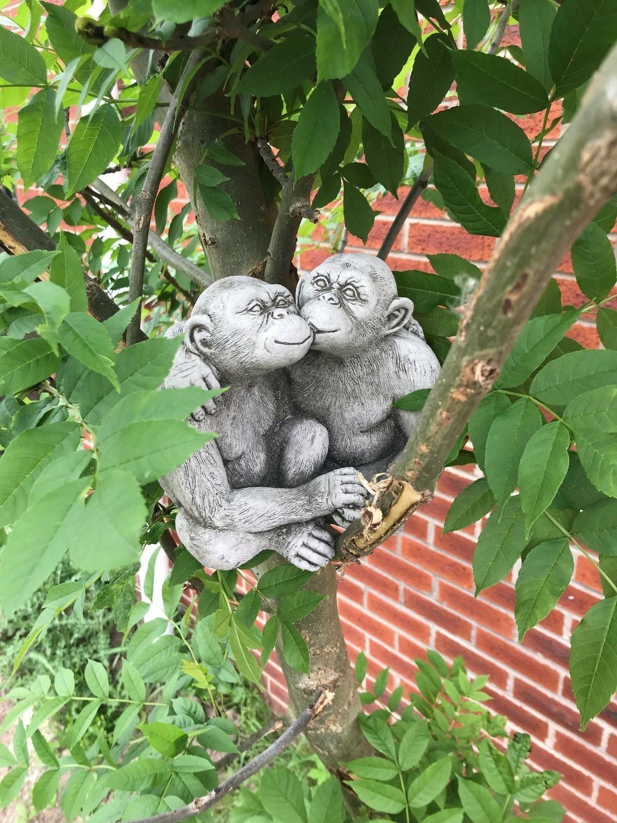 Charming Stone Kissing Monkey Couple nestled in tree branches, ideal for whimsical garden or patio decoration.