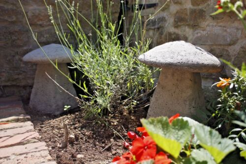Garden Decor - Stone Staddle Toadstool Ornament placed among flowers and greenery. Durable, weatherproof garden ornament with antique grey finish.