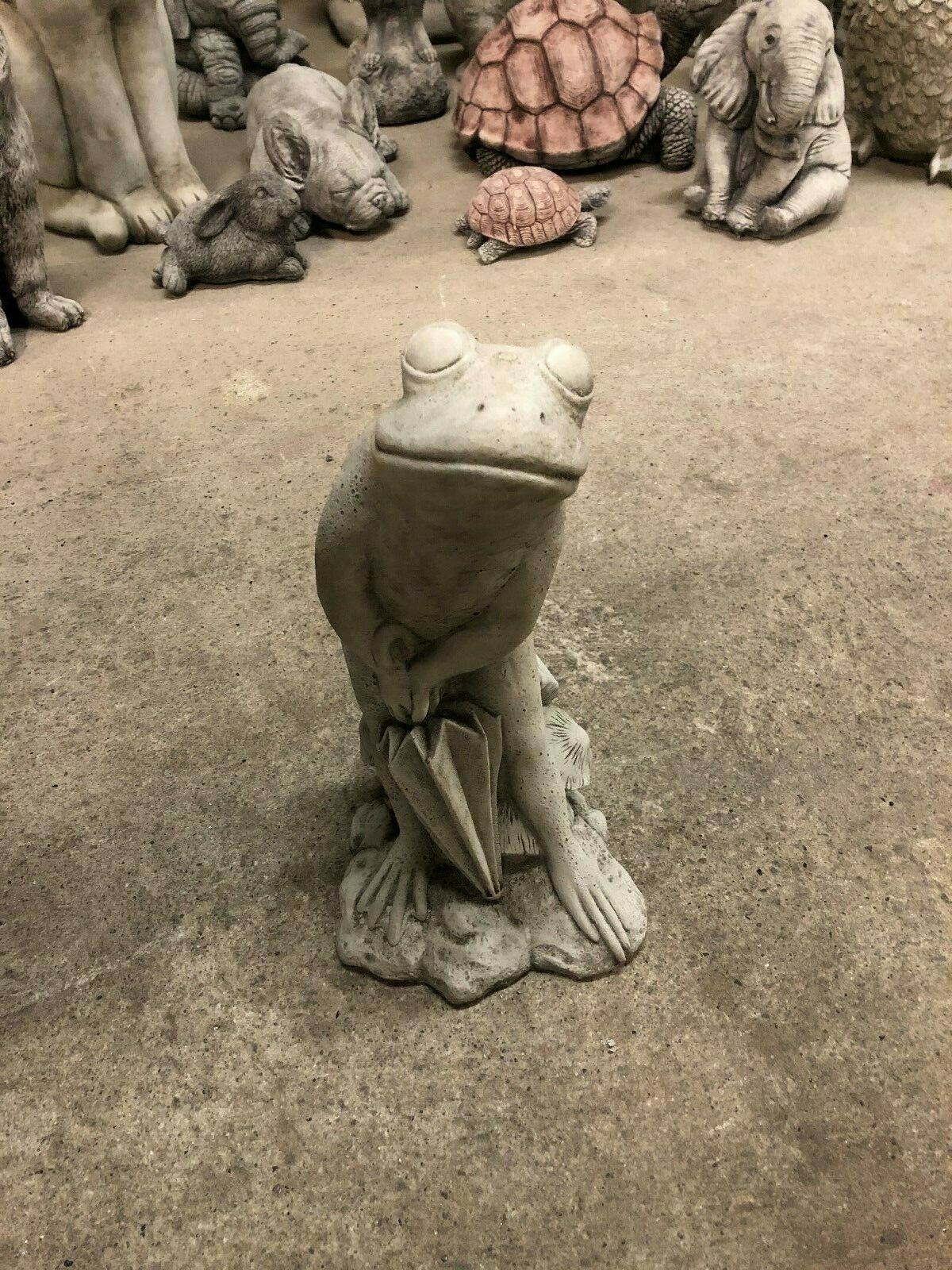Front view of Elegant Stone Frog Garden Ornament holding an umbrella, surrounded by other animal statues in a showroom setting.