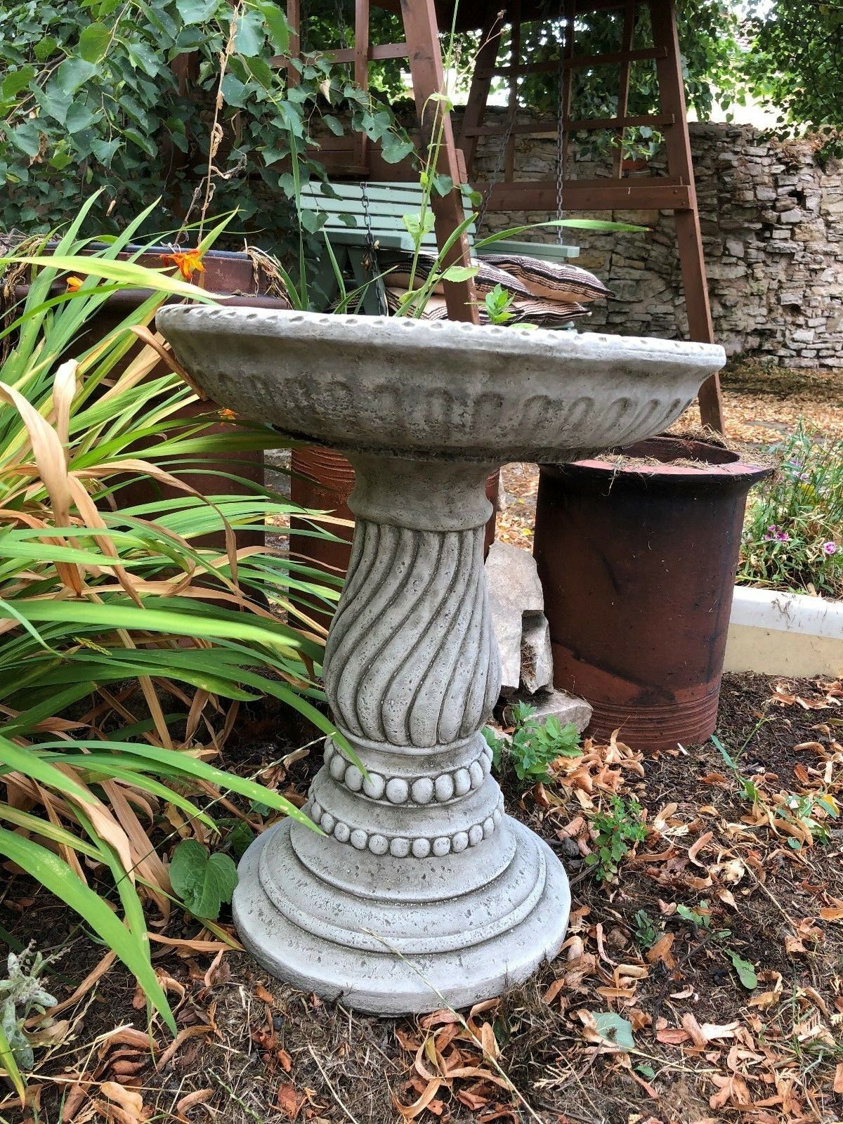 Outdoor stone bird bath with elegant twist base and beaded detailing, perfect for gardens and patios. Made from weather-resistant limestone.