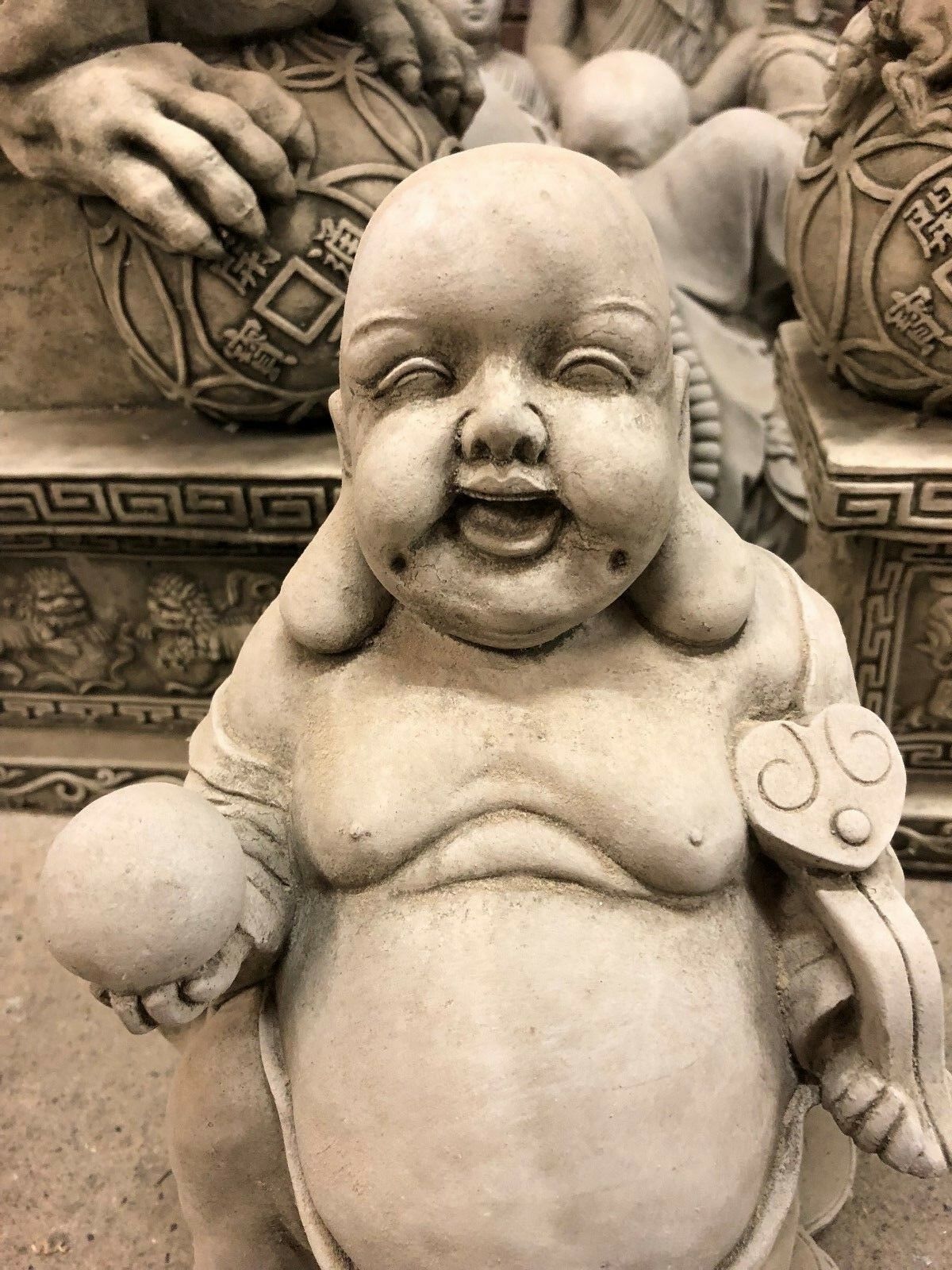Close-up of Wealth Buddha Garden Statue with serene smile and prosperity ball, crafted in durable stone for garden settings.