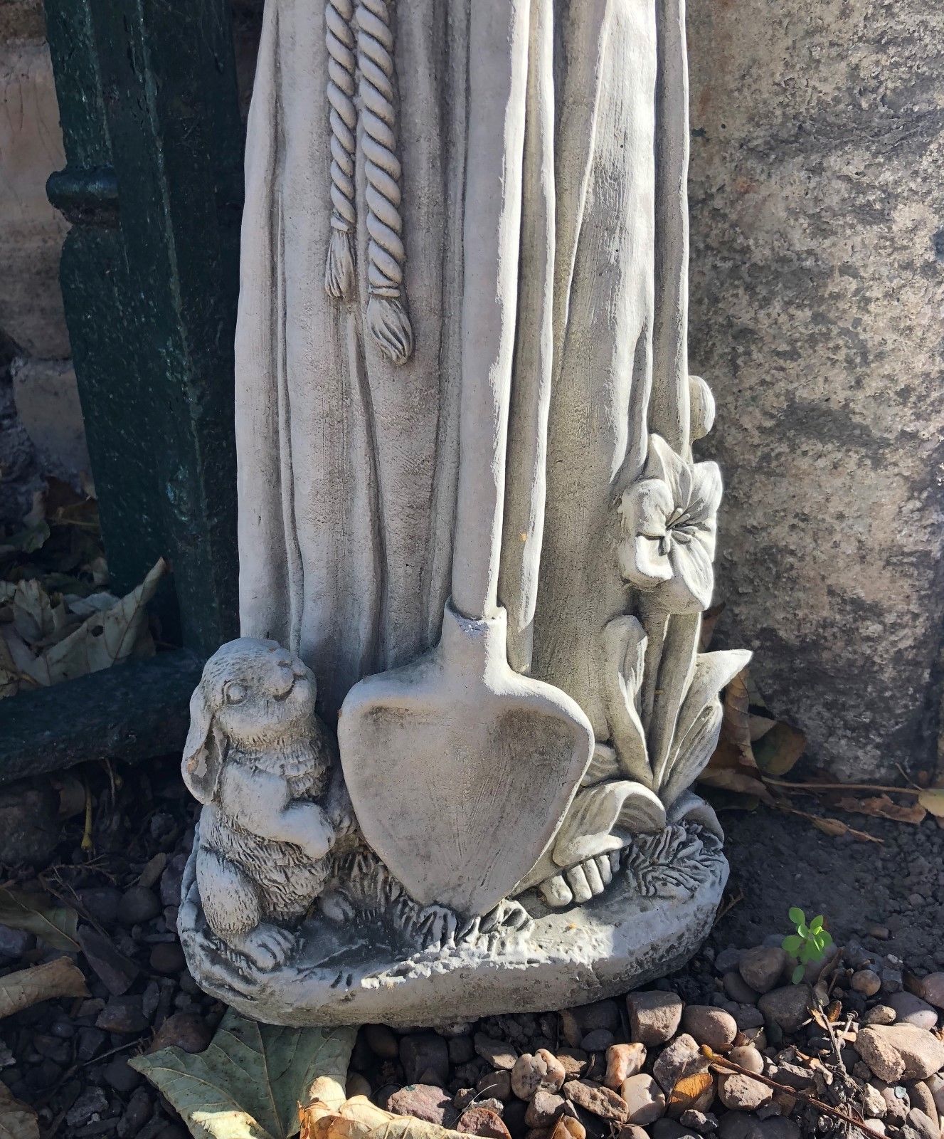 Base of St Francis garden statue with rabbit, shovel, and flower details. Stone sculpture suited for garden beds or outdoor sanctuaries.