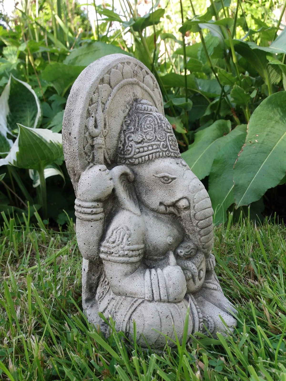 Side view of Small Stone Ganesh Garden Ornament on grass. Durable and weatherproof, perfect for outdoor spiritual decoration.