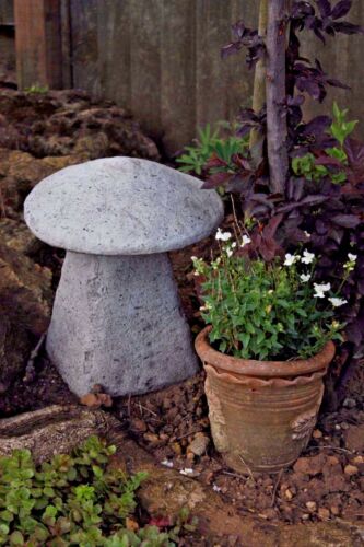 Stone Staddle Toadstool Ornament next to a potted plant in a rustic garden. Handmade garden decor ideal for outdoor patios and flower beds.