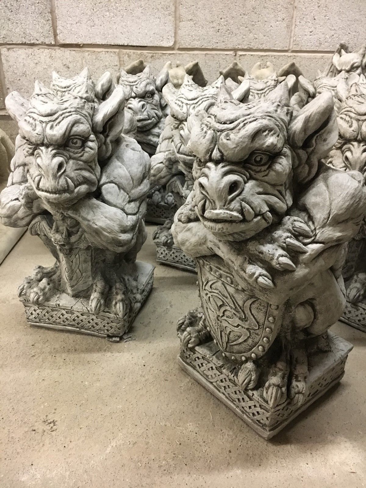 Pair of stone gargoyle statues holding shields and swords, crafted from durable limestone for garden ornamentation with antique charm.