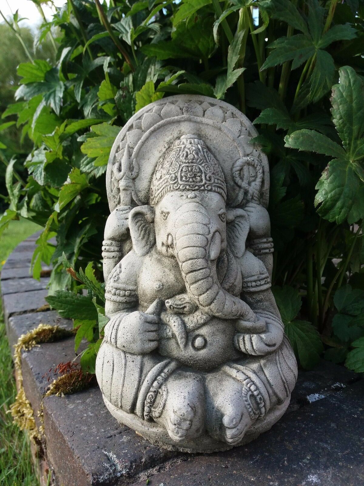 Front-facing Ganesh Garden Ornament - Small Stone placed on a brick edge. Detailed limestone sculpture for garden or patio.