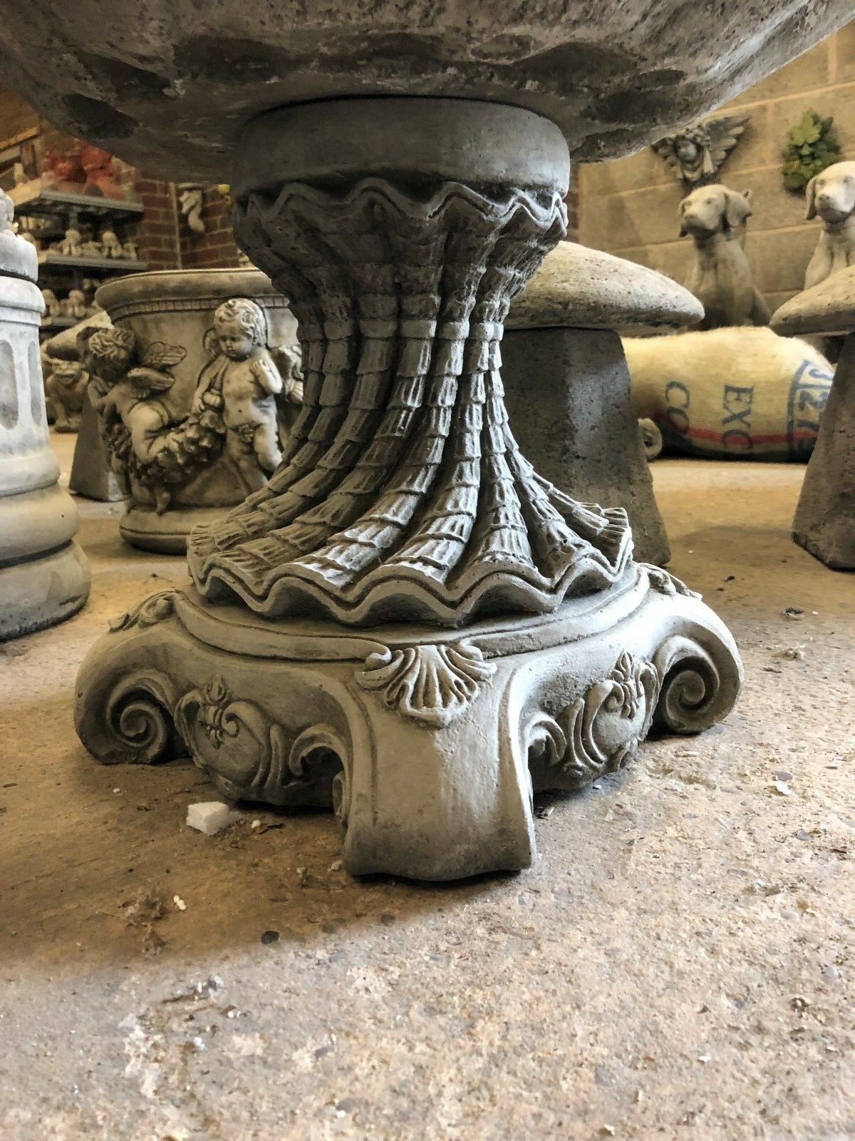 Detailed view of the twisted pedestal base of the Stone Shell Bird Bath, emphasizing its ornate stone carvings and solid build.