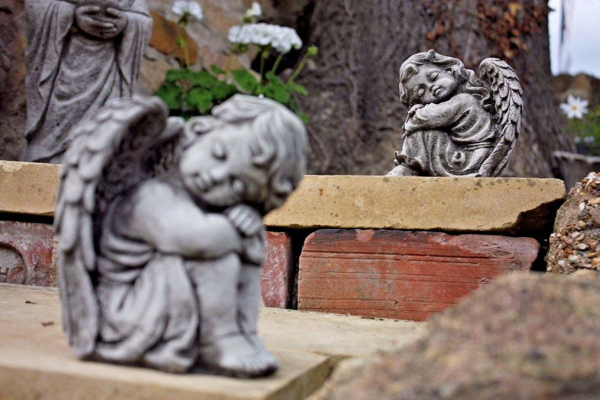 Two stone angel garden ornaments placed on brick and stone steps with flowers in the background. Weather-resistant statues for outdoor spaces.