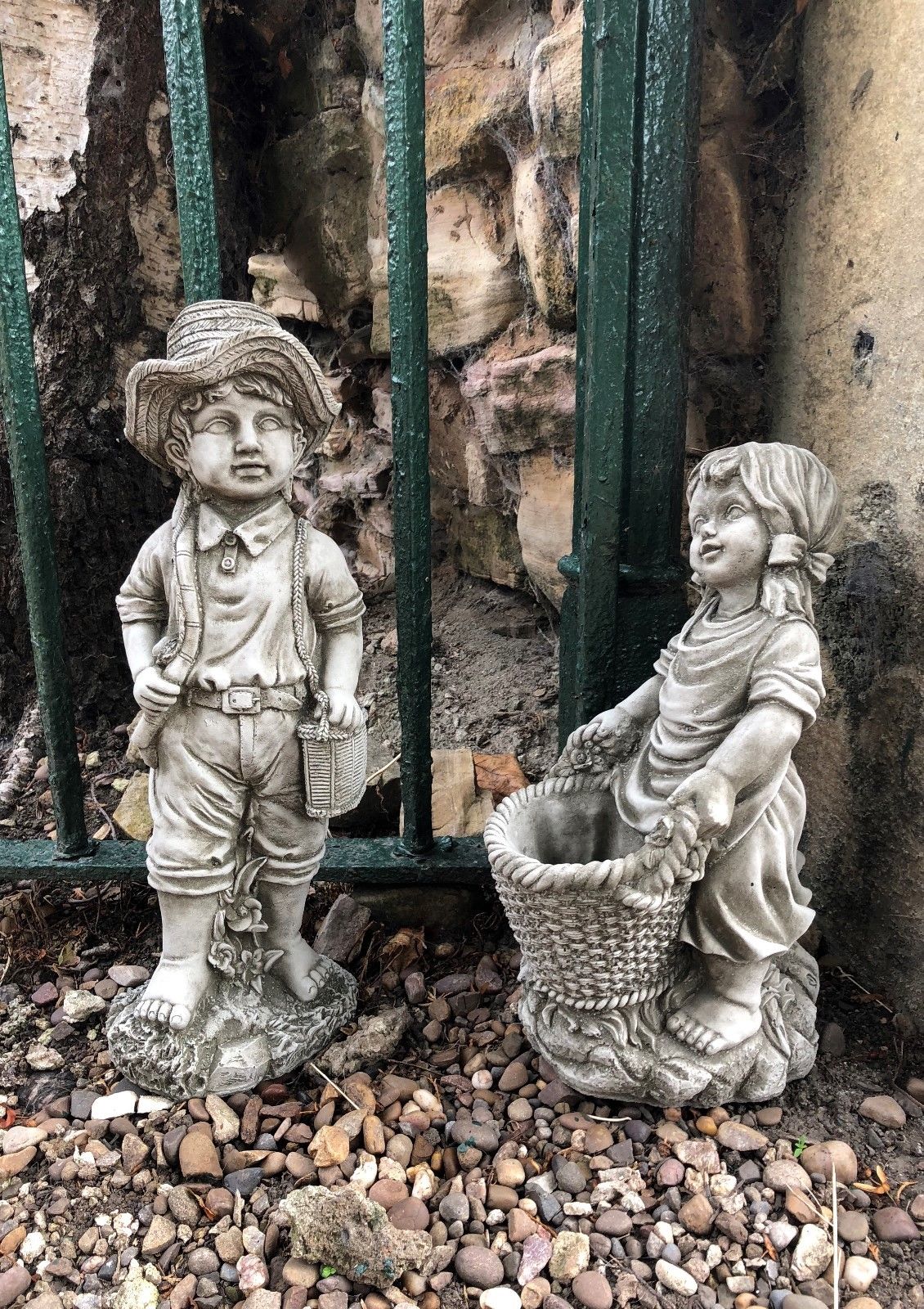 Fisher boy and basket girl garden statues with antique stone finish, ideal for lawn or flowerbed decor in outdoor garden settings.