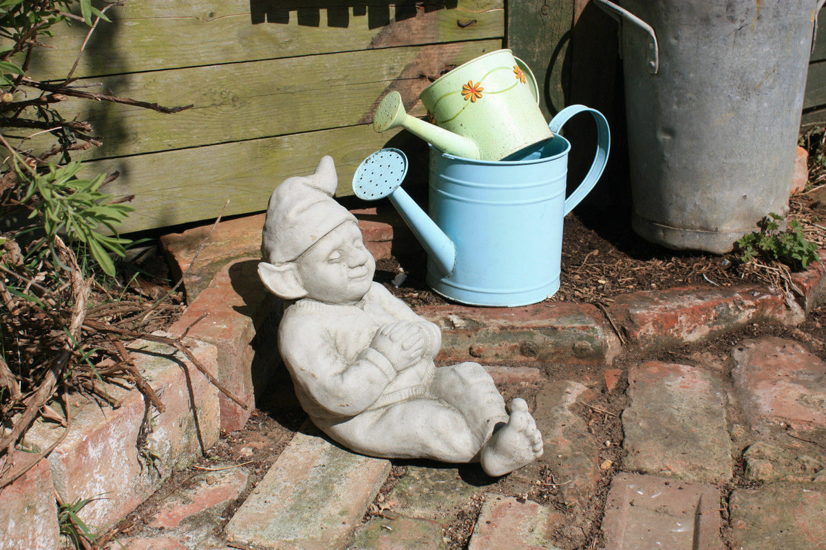 Garden Gnome Ornament - Relax outdoors | Durable & Antique Finish, resting on brick path near watering cans, ideal for rustic garden decor.
