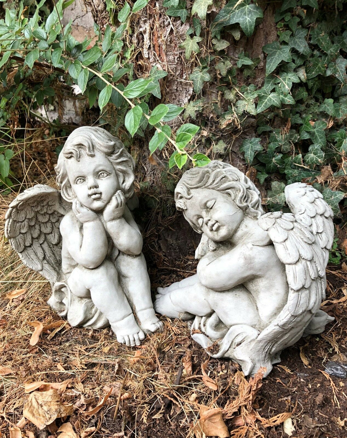 Pair of stone winged baby angel sculptures in resting poses. Perfect for garden decor, spiritual spaces, or outdoor memorials.