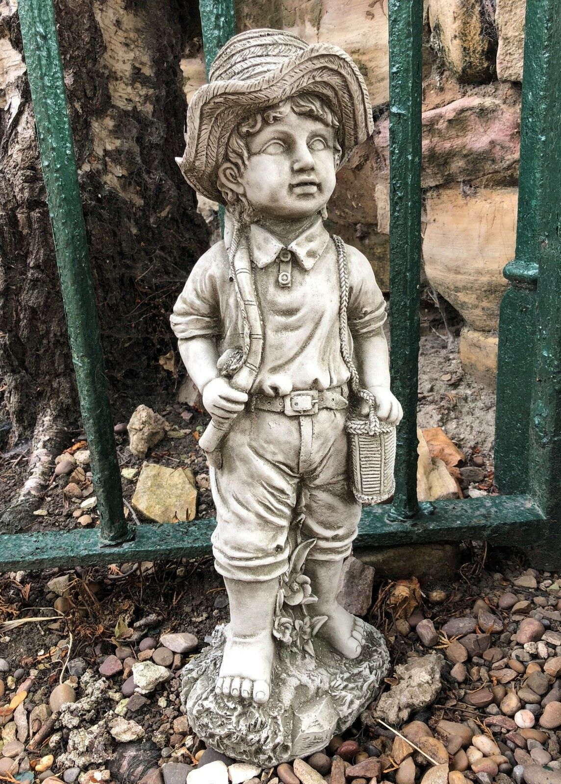 Close-up of stone fisher boy garden ornament with fishing rod and basket, detailed craftsmanship perfect for rustic garden decor.
