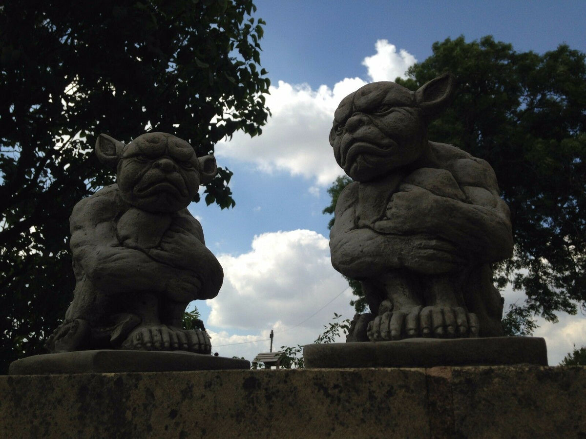 Grumpy Stone Gargoyles silhouetted against blue sky, ideal for outdoor decor. Durable limestone statues for garden or patio display.