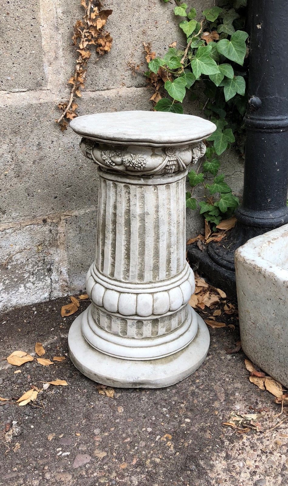 Detailed view of stone pedestal with floral carvings and fluted design, suitable for supporting garden statues or planters.