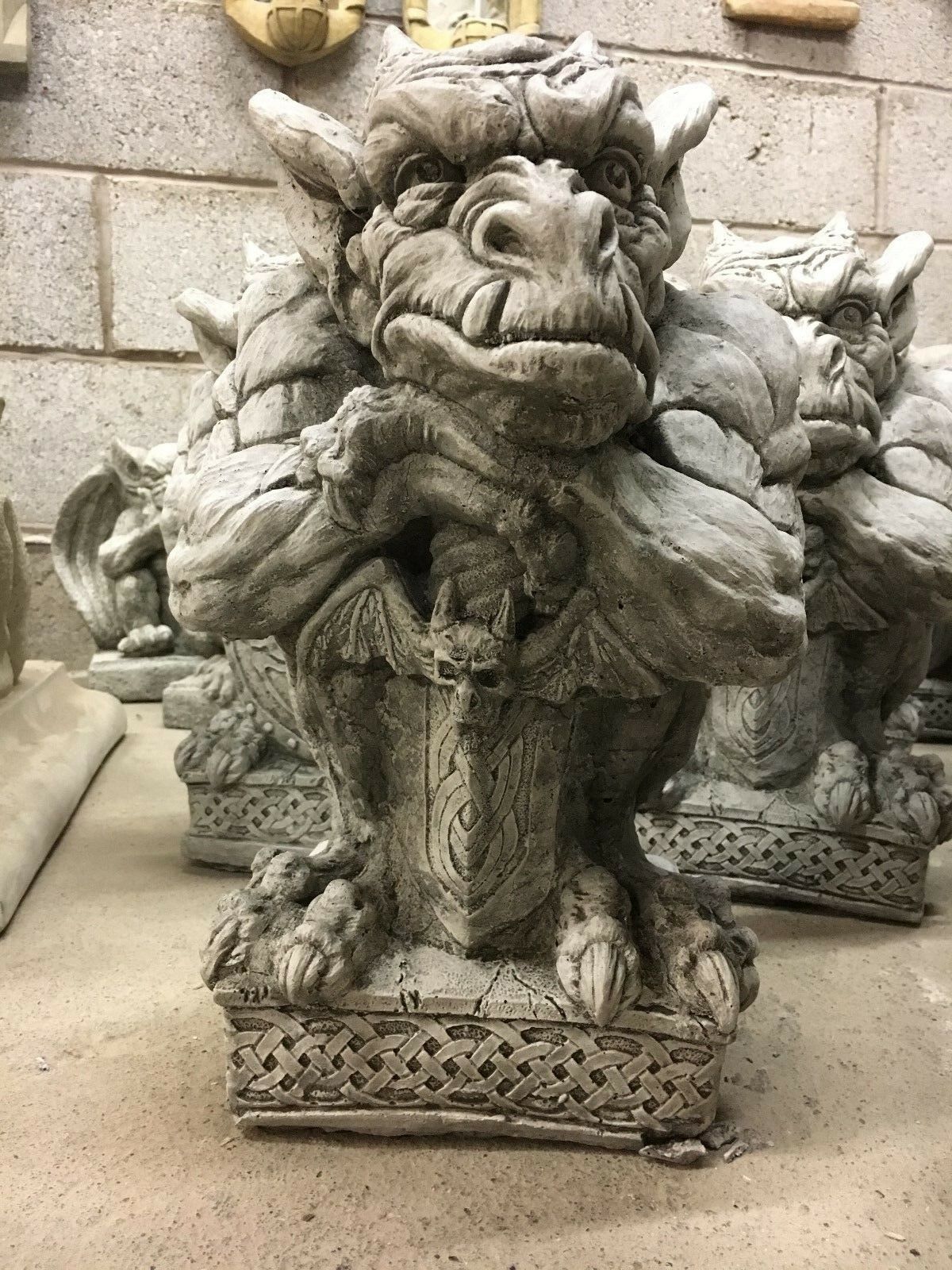 Close-up of a stone sword shield gargoyle statue showing muscular arms and gothic shield design, ideal for enhancing garden aesthetics.