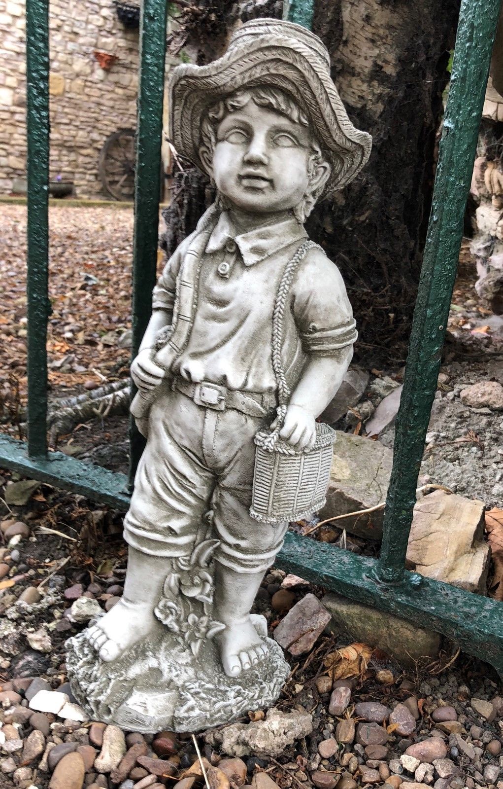 Side view of fisher boy garden statue in antique stone finish, holding a fishing rod and basket, ideal for outdoor garden sculpture.