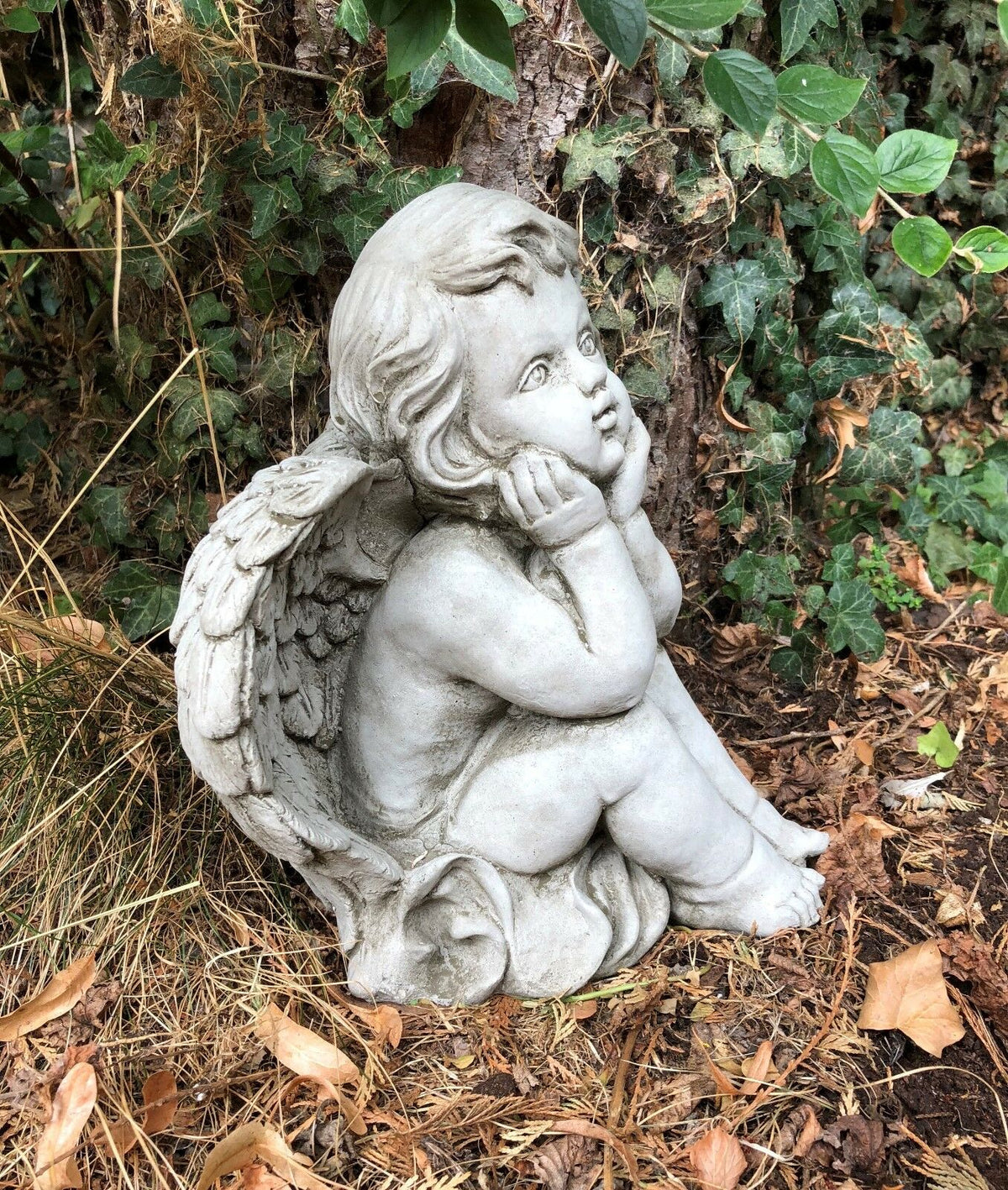 Side view of thoughtful stone baby angel with wings. Durable outdoor sculpture for garden or spiritual decor.