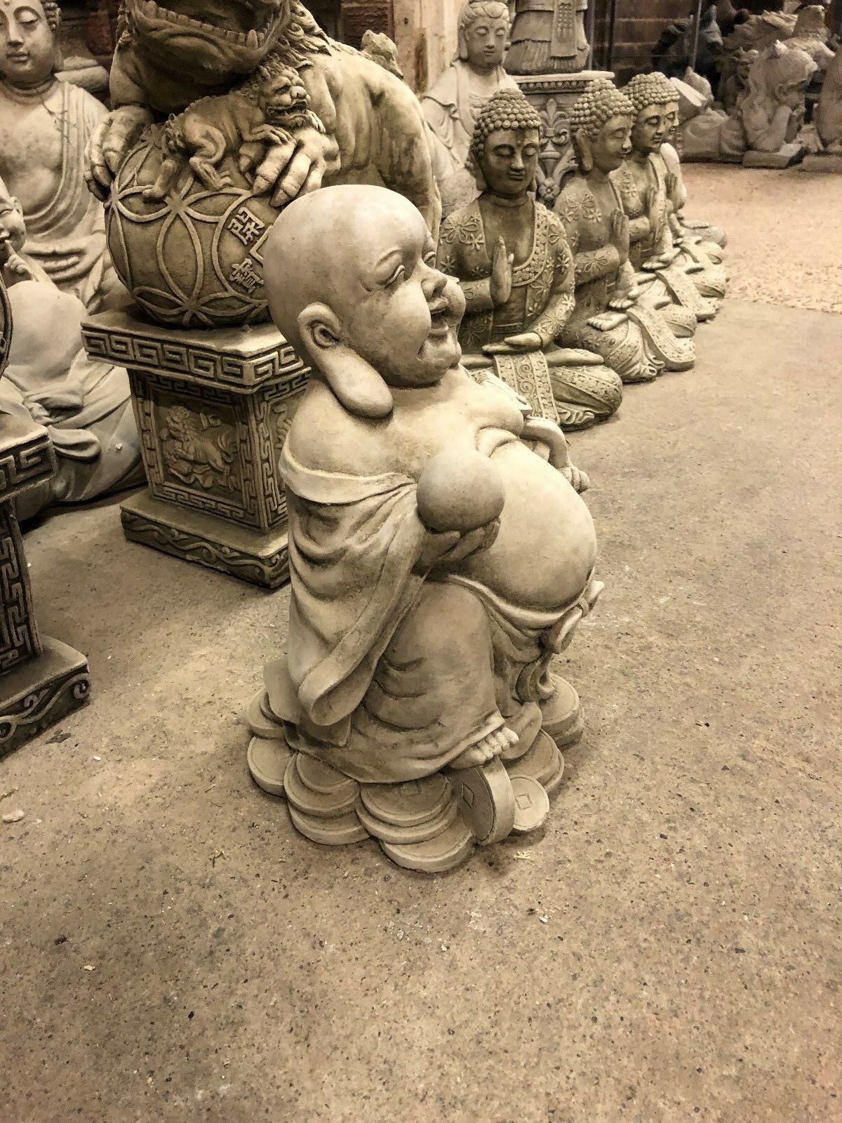 Angled view of Wealth Buddha Garden Statue with joyful expression, seated on coins, perfect for patio or garden display.
