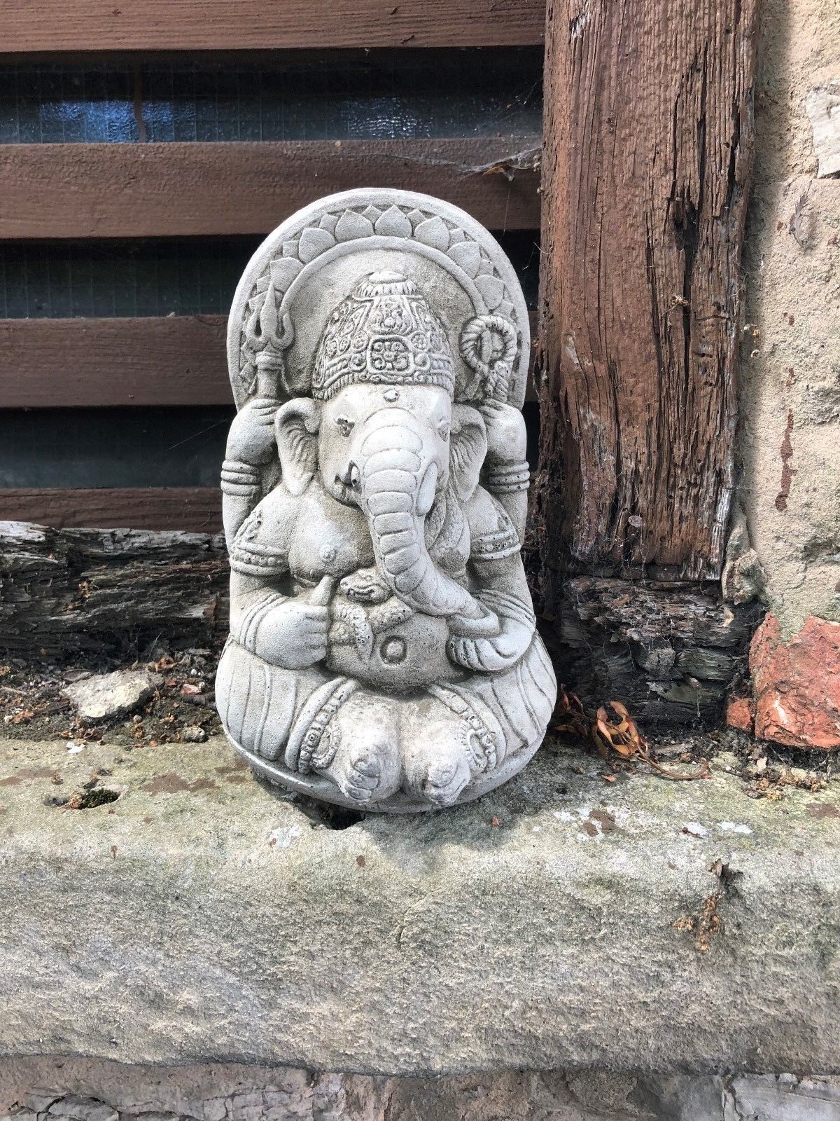Small Stone Ganesh Garden Ornament placed on a rustic stone ledge. Weatherproof and ideal for outdoor spiritual ambiance.