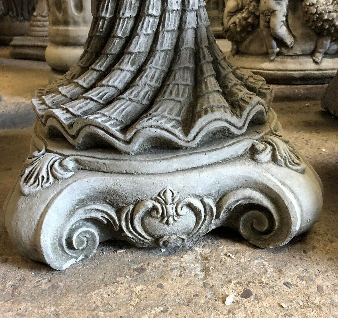 Close-up of the decorative base of the Stone Shell Bird Bath, featuring scrollwork and antique-style stone detailing.