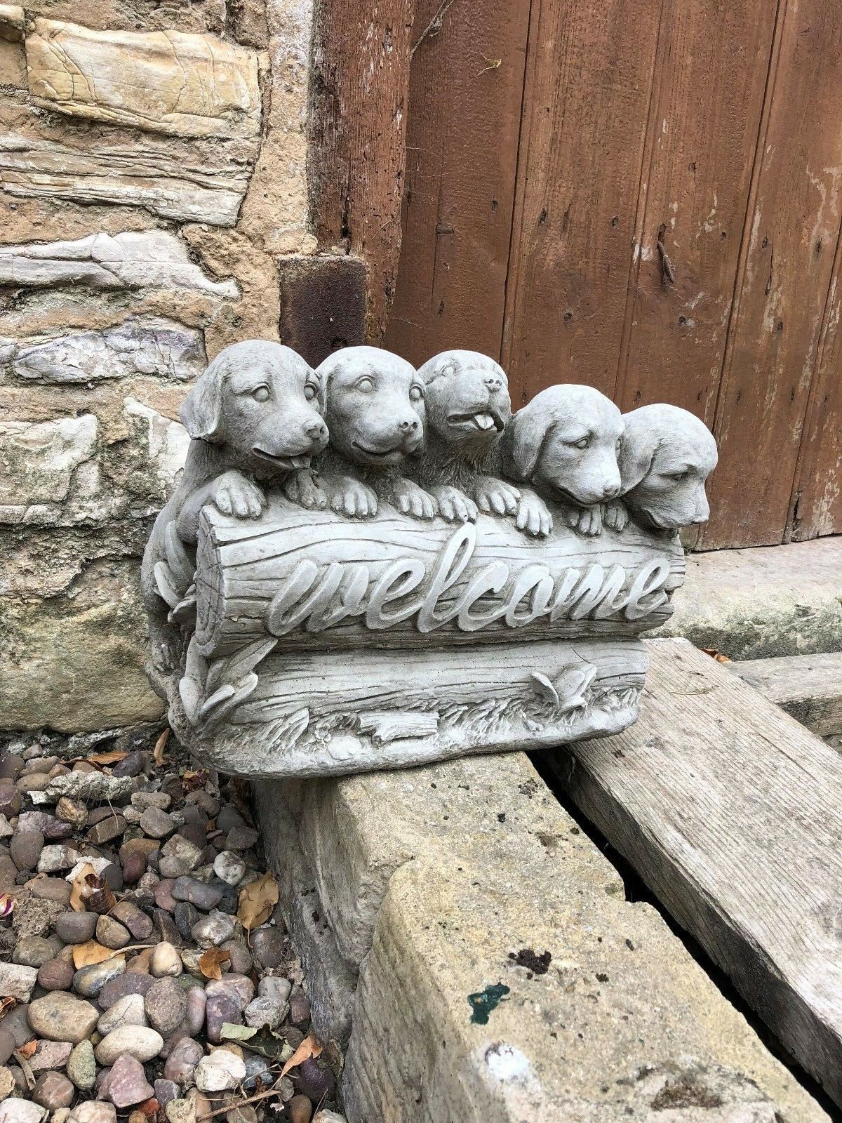 Charming stone garden ornament with five puppies and welcome sign, placed on rustic stone steps for outdoor decor.
