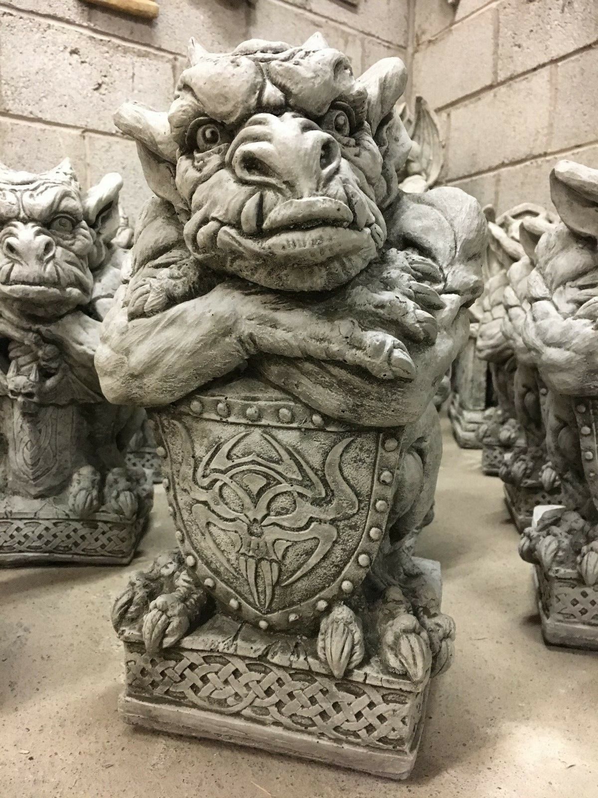 Front view of a limestone gargoyle statue with sword and shield, showcasing intricate carvings for a bold garden centerpiece.