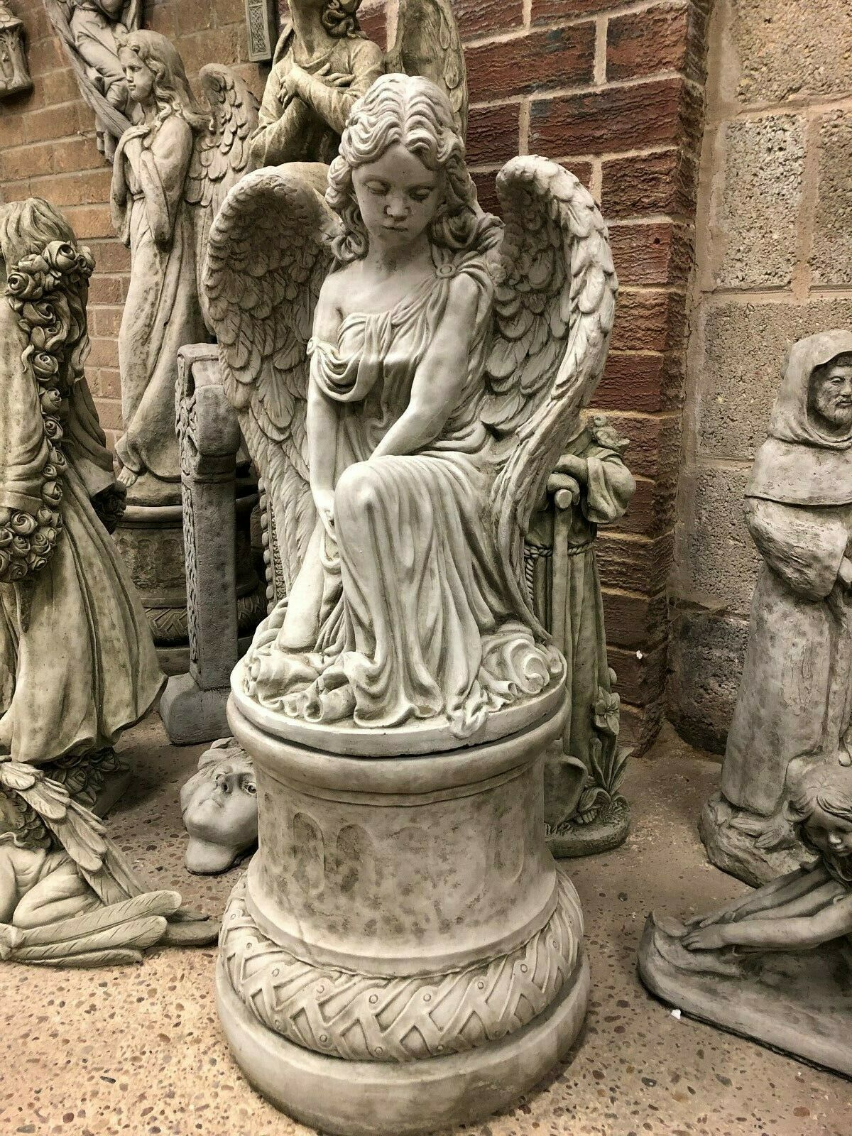 Elegant Stone Angel Garden Pedestal Statue for Landscaping. Graceful angel figure with flowing gown and feathered wings, perfect for garden ornamentation.