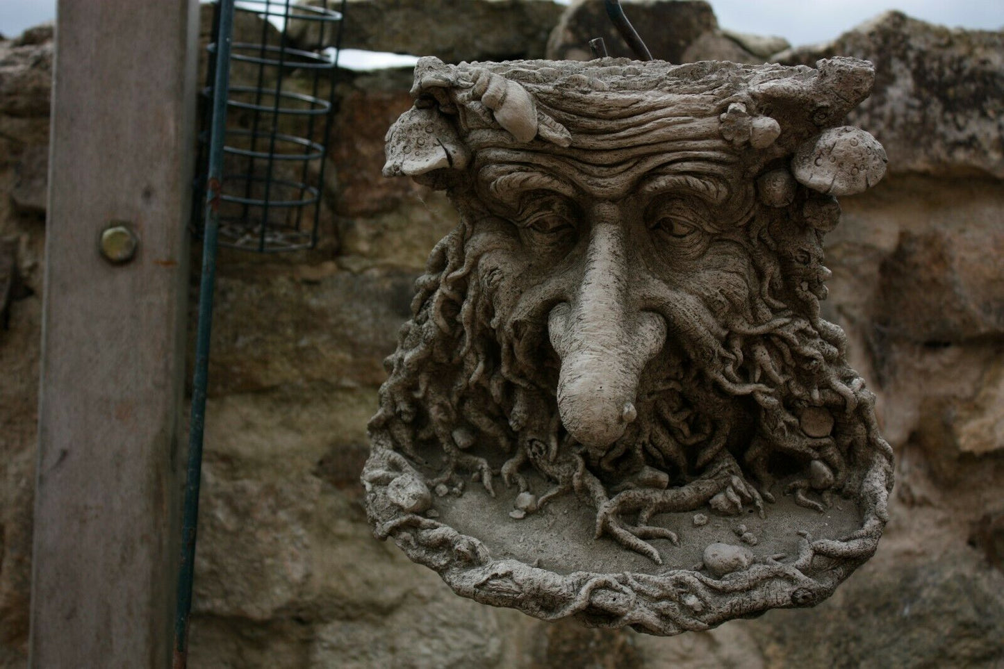 Durable Long Nose Greenman Bird Feeder Stone Ornament hanging on a stone wall, ideal for outdoor garden decoration and bird feeding.
