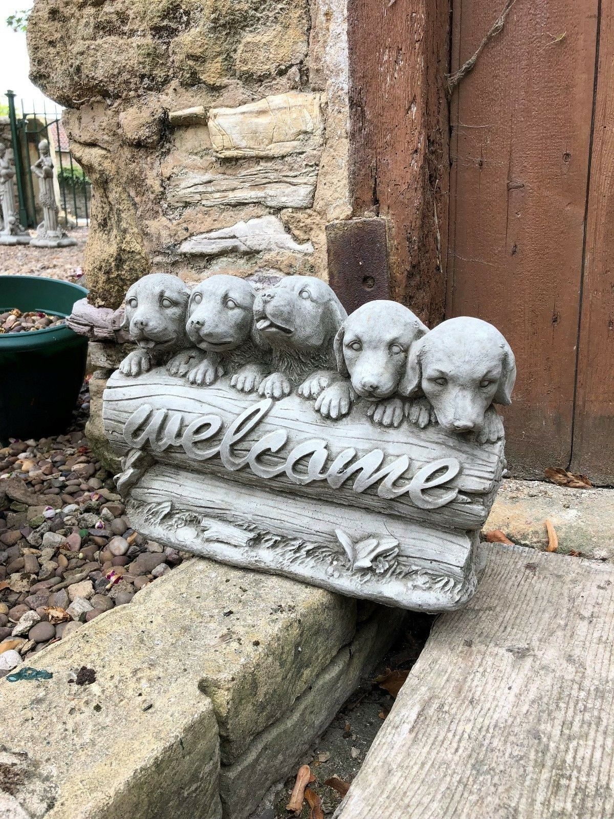 Decorative stone welcome puppies garden sculpture leaning against a wooden door, ideal for home and garden use.