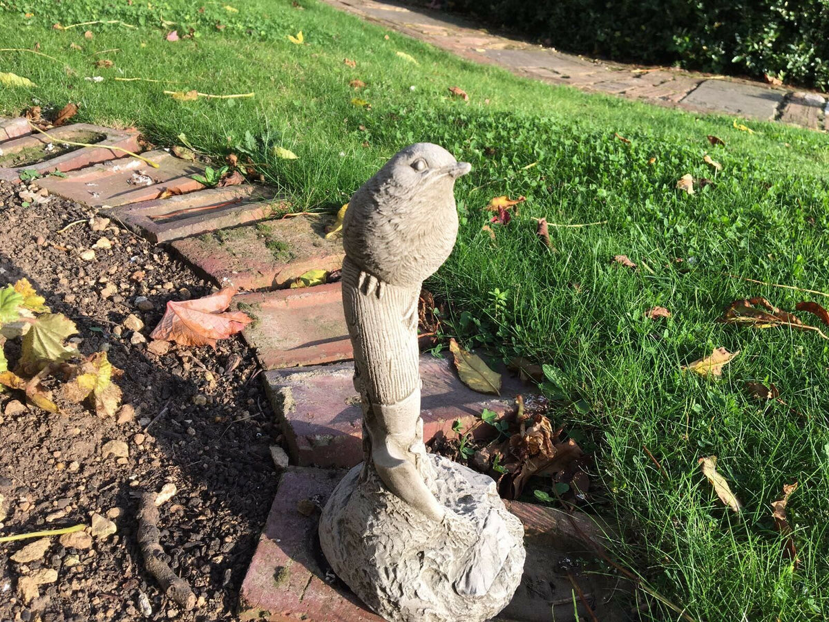 Side view of Stone Bird Garden Ornament on Spade set on a lawn edge. Handmade limestone sculpture for garden decoration.