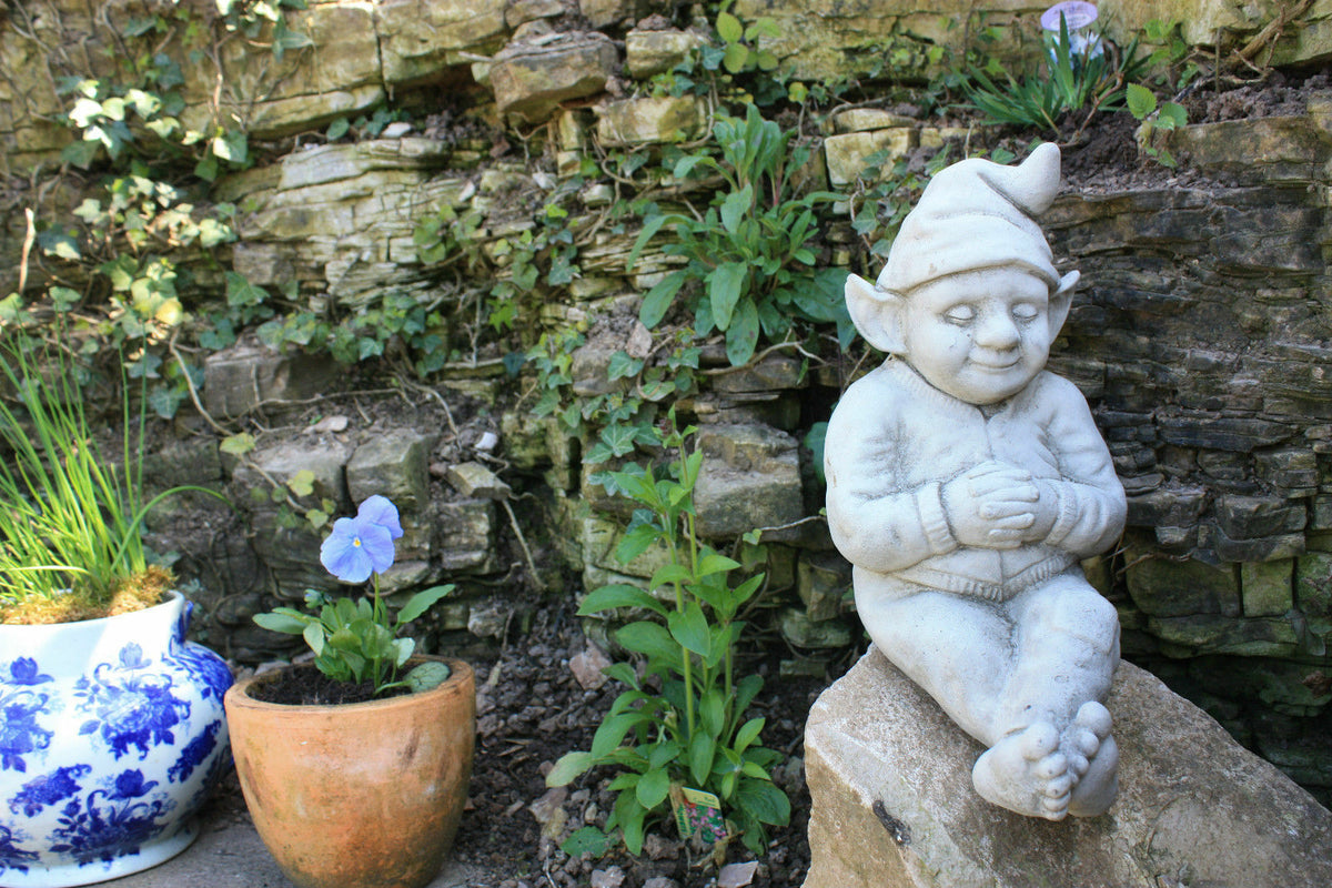 Garden Gnome Ornament - Relax outdoors | Durable & Antique Finish, seated on stone ledge near plants, enhances natural garden aesthetics.