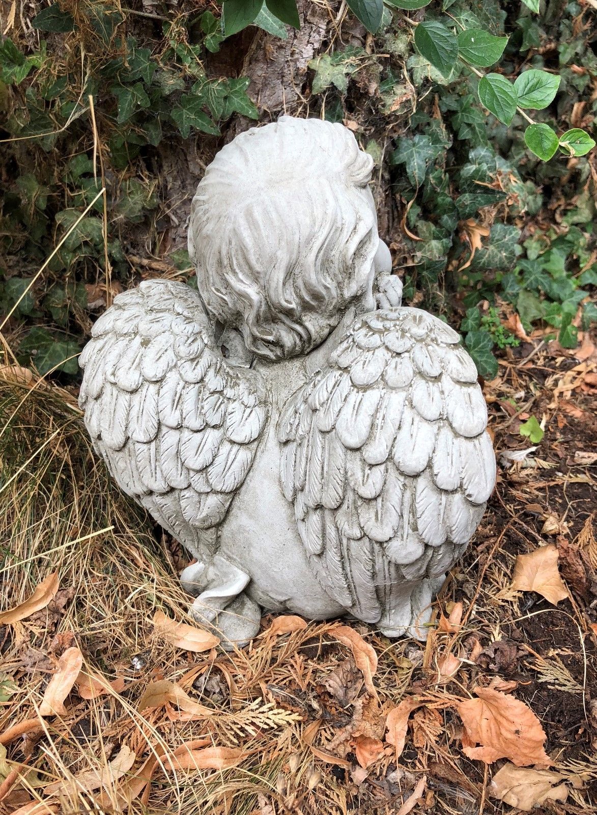 Back of stone cherub showing intricate wing texture. Weatherproof garden ornament for year-round outdoor display.