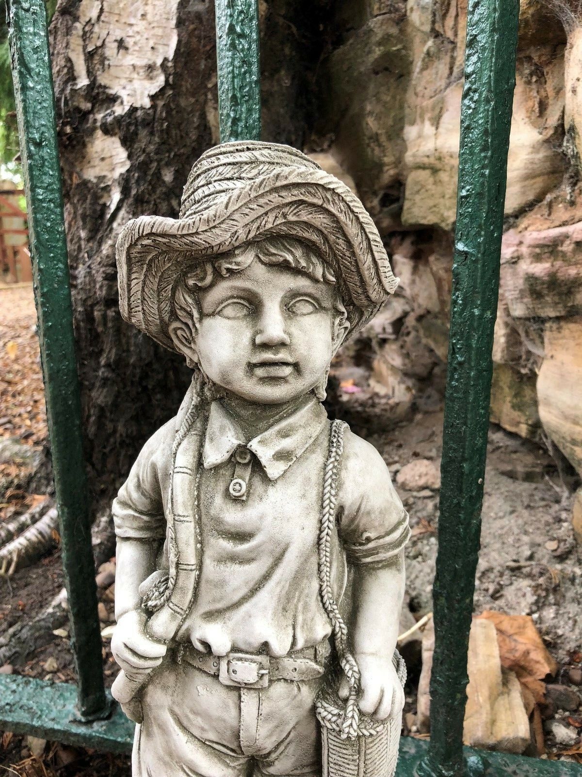 Upper detail of fisher boy garden sculpture showing textured hat and facial features, made from durable stone for garden decoration.