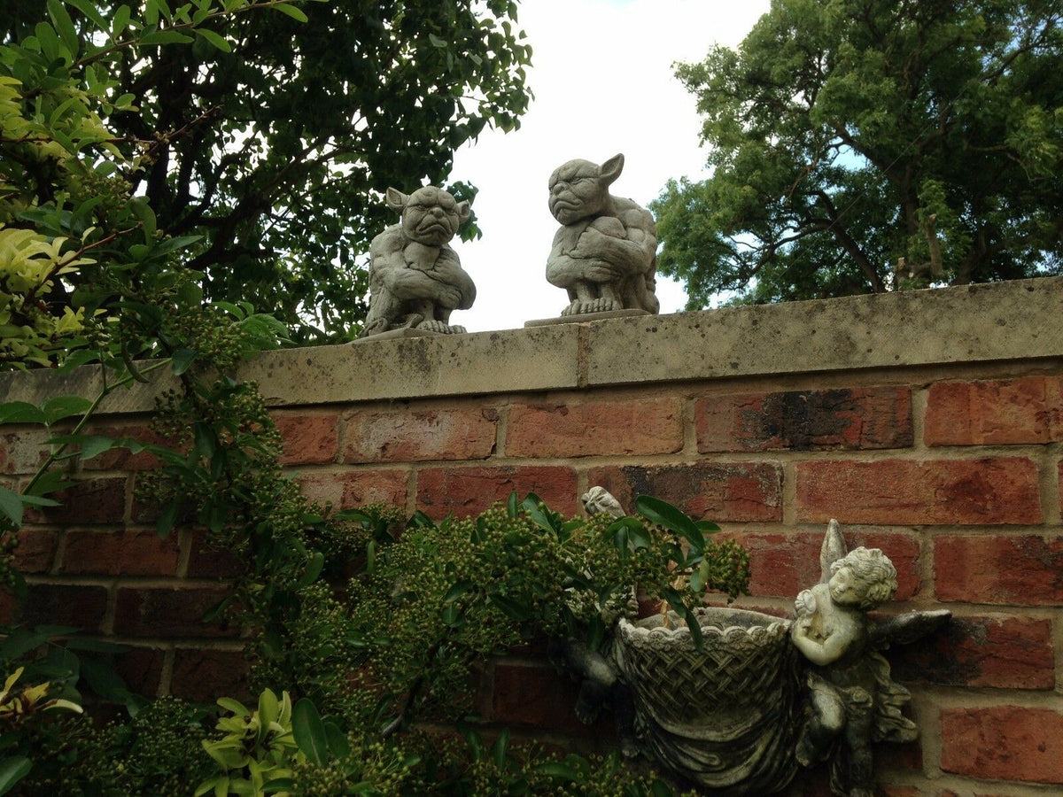 Outdoor Grumpy Gargoyle Statues on garden wall above angel planter. Unique gothic decor for home and garden spaces.
