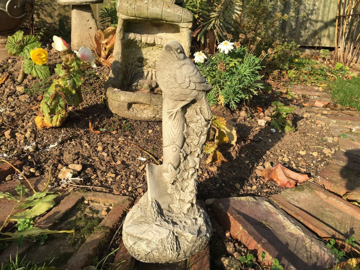 Stone Bird Garden Ornament on Spade with ivy carvings, positioned in a rustic garden. Durable and charming lawn sculpture.