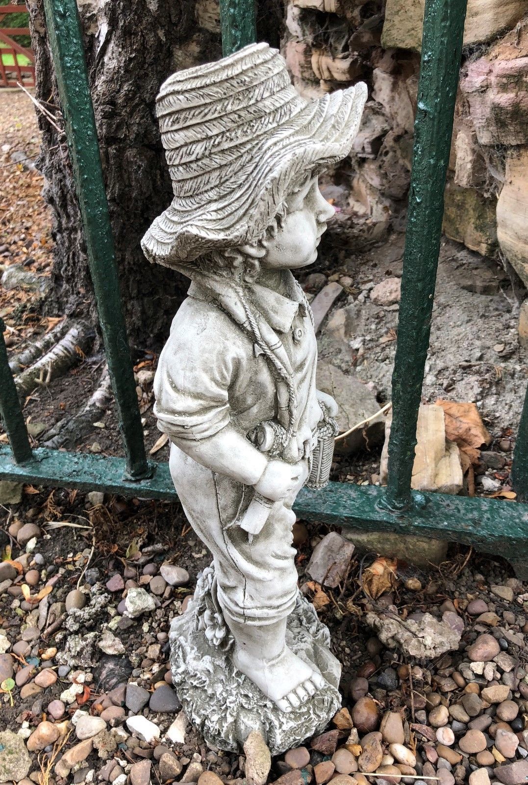 Side profile of fisher boy garden statue with fishing rod and basket, crafted in stone for outdoor lawn or flowerbed display.