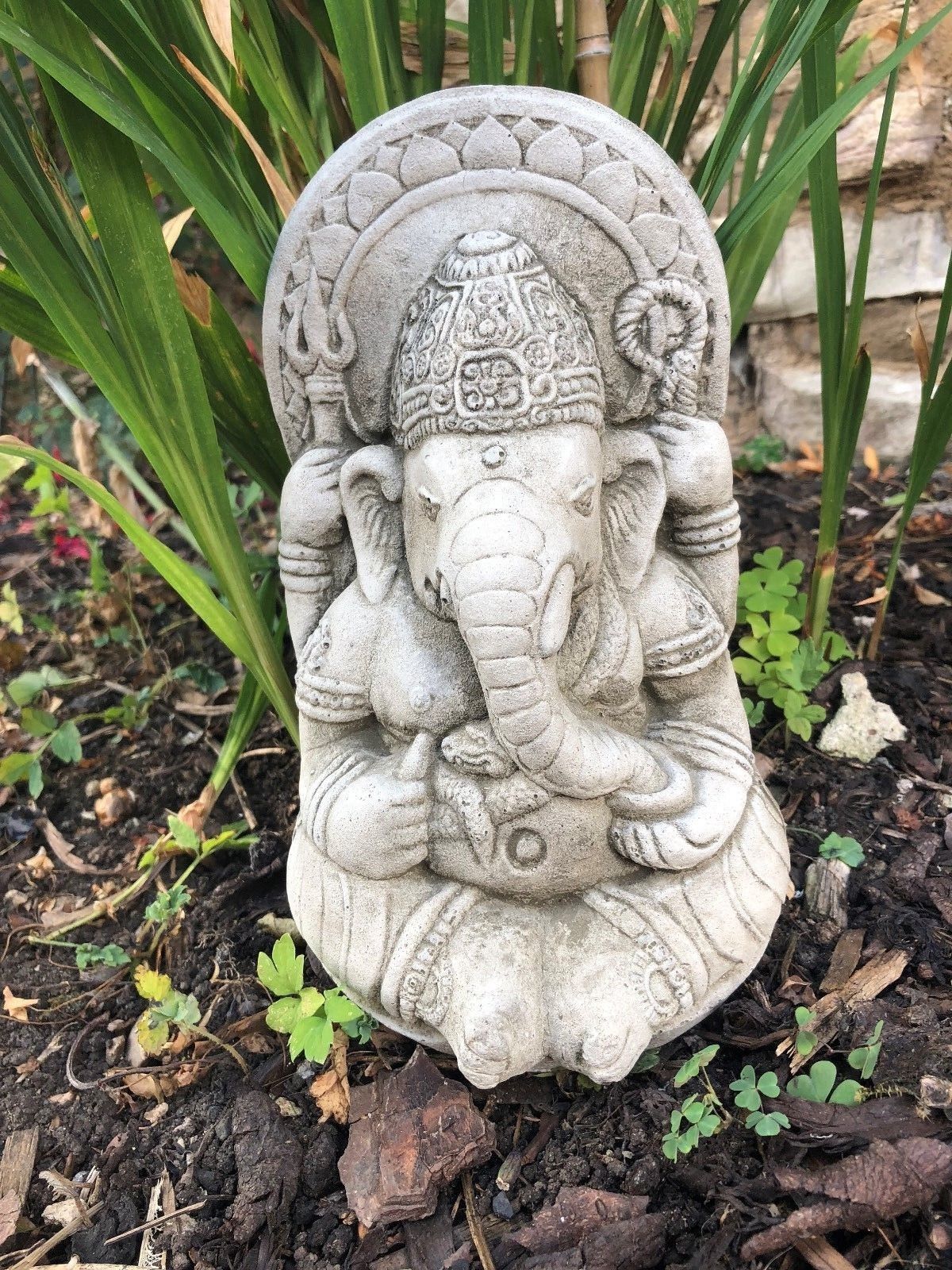 Close-up of Small Stone Ganesh Garden Ornament in a flower bed. Weatherproof and intricately detailed for outdoor settings.