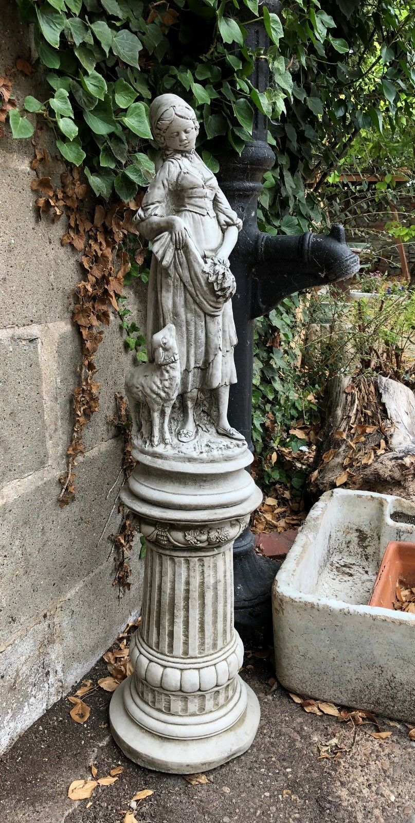 Elegant Stone Garden Shepherdess Statue with lamb on classic pedestal, enhancing garden ambiance with timeless sculpture design.