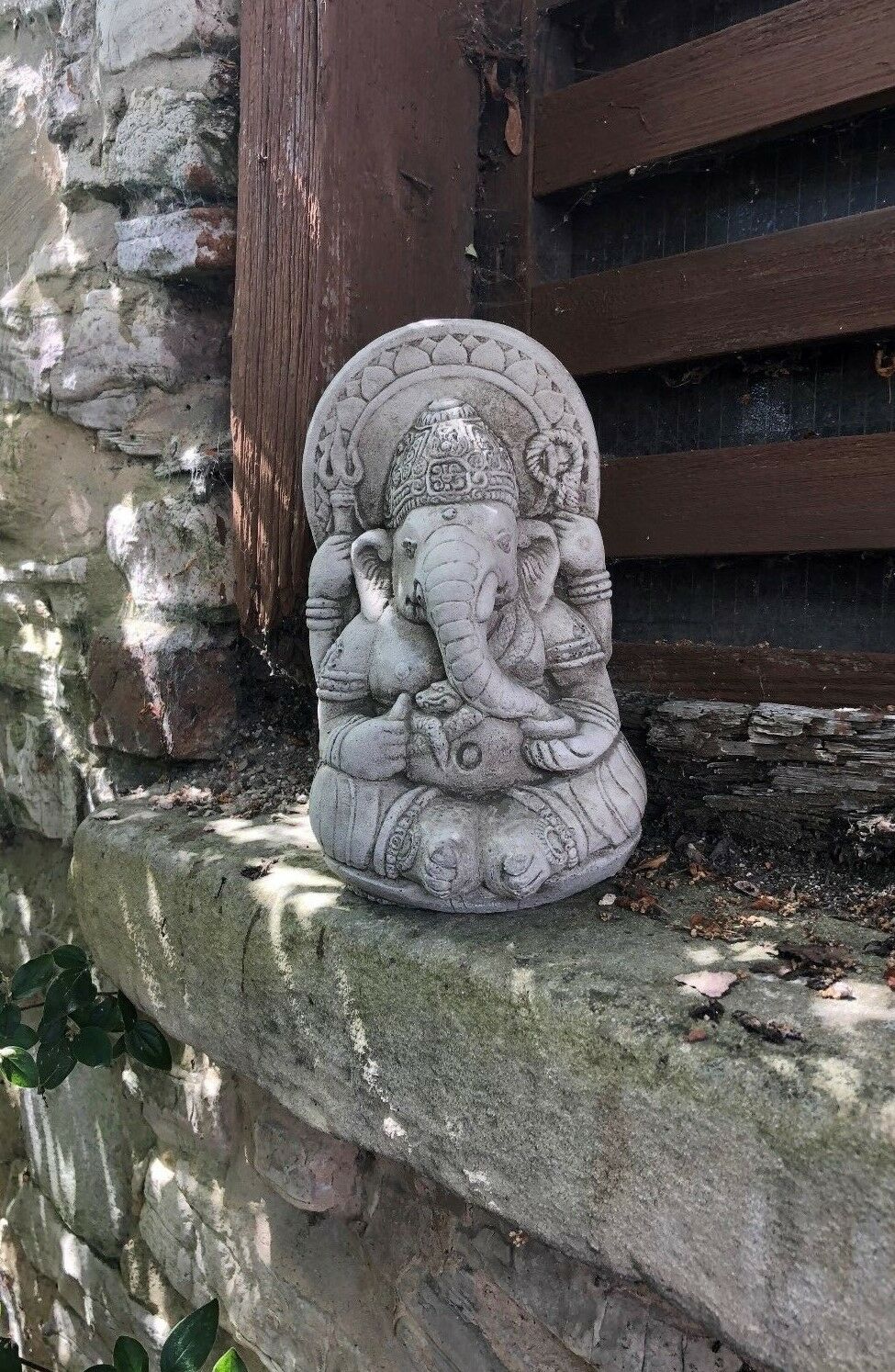 Ganesh Garden Ornament - Small Stone on a stone ledge near a wooden wall. Ideal for spiritual garden or patio decor.