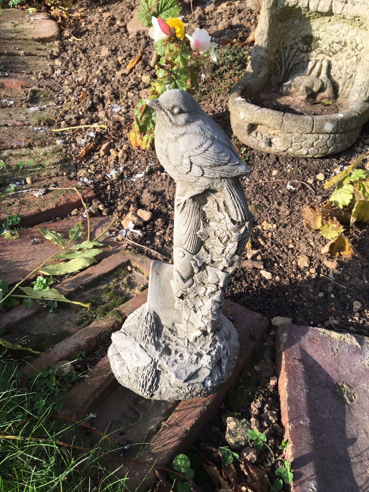 Handcrafted Stone Bird Garden Ornament on Spade in a landscaped garden. Perfect for adding charm to outdoor spaces.